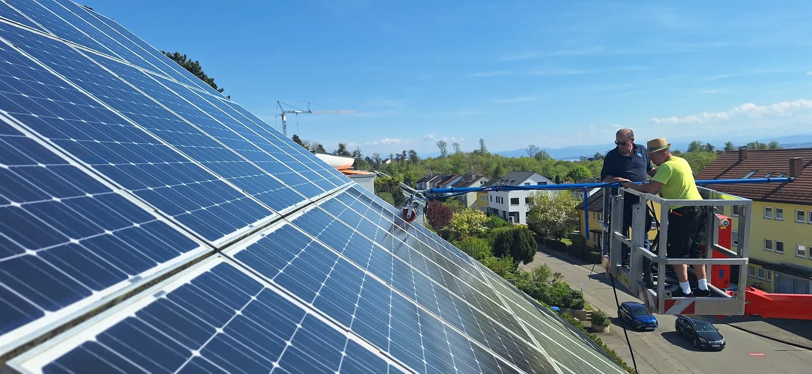 Zwei Mitarbeiter reinigen ein Solardach von einer Hebebühne aus